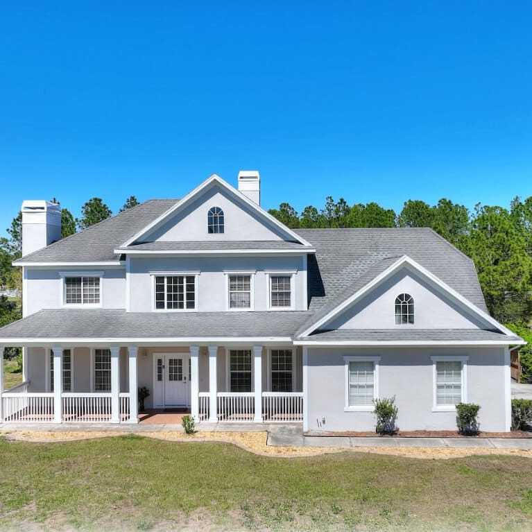 White two-story stucco home with columned front porch repainted by painters in St. Cloud