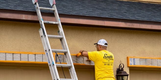 Two Smith and Co. painters in yellow shirts prepping and painting a home exterior